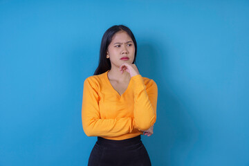 Young woman is pondering with her hand on her chin, deep in thought against a blue background
