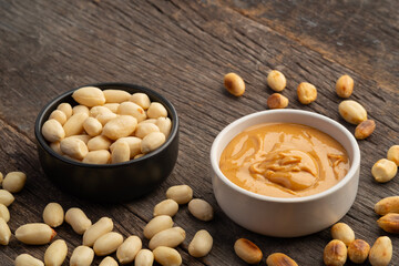 Creamy and smooth peanut butter in white bowl with peeled groundnut scattered.
