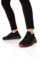 Dynamic close-up of a young woman's legs wearing black athletic sneakers with pink soles, paired with black slim-fit pants, sleek and stylish footwear, minimalist background, comfortable sneakers.