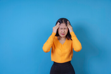 Young woman holding her head with her hands, grimacing from pain, suffering from a headache on blue background