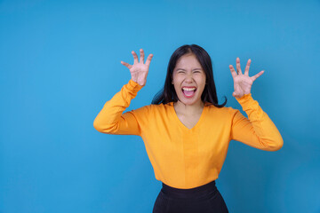 Young woman is playfully making a scary face, with her hands raised like claws and a mischievous grin