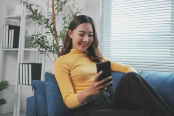 Young asian businesswoman using smartphone and relaxing on sofa with happiness, work at home concept