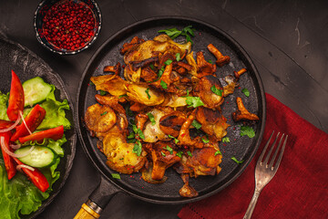 Chanterelle mushrooms fried with potatoes according to a traditional recipe in a cast-iron pan on a dark table with a burgundy napkin, with vegetables and berries