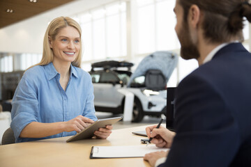 Happy woman signing contract for the purchase of car in showroom