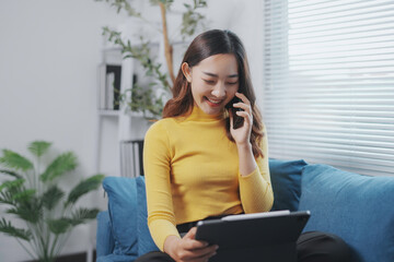 Young woman is working remotely, having a pleasant phone call while using her digital tablet, sitting comfortably on the sofa © Crystal