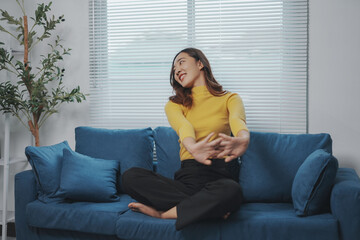 Obraz premium Young woman is sitting on her couch at home, stretching her arms and upper body