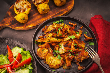 Vegetarian dinner: chanterelle mushrooms with potatoes in a cast-iron pan, stuffed pumpkins on a wooden board and vegetables on a dark table. with a burgundy napkin.
