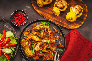 Vegetarian dinner: chanterelle mushrooms with potatoes in a cast-iron pan, stuffed pumpkins on a wooden board and vegetables on a dark table. with a burgundy napkin.