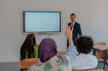 In the classroom group of college students listening to a university lecturer and engages in discussion and debate. Student raising a hand with a question for the teacher.