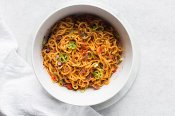 Overhead view of Spicy instant noodles with slices of green and red chili, spicy ramen noodles in a white ceramic bowl