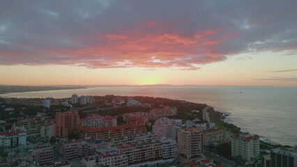 Colorful sunrise lighting coastal town washed by picturesque ocean aerial view