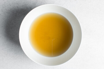 Overhead view of chicken broth in a white bowl, top view of cooked chicken beef broth, process of...