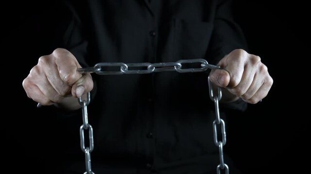 Person hands fight with chain in night. A view of man hands fighting with emotions with metal chain against black background.