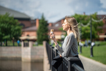 Relaxed girl having good time outdoors outside snacking on delicious sweet ice cream in waffle cone. Woman leaning on railing while resting by water on bridge, eating yummy dessert on walk, stroll