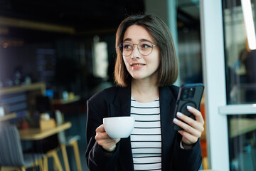 Businesswomen with coffee working on laptop in office, happy beautiful businesswomen in formal suit working at workplace. Emotions of a woman in the office.