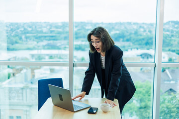 Obraz premium Businesswomen with coffee working on laptop in office, happy beautiful businesswomen in formal suit working at workplace. Emotions of a woman in the office.
