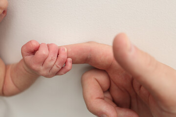 The newborn baby has a firm grip on the parent's finger after birth. Close-up little hand of child and palm of mother and father. Parenting, childcare and healthcare concept.