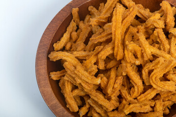 A heap of spicy soy stick snack from India in carved wooden bowl, isolated on white