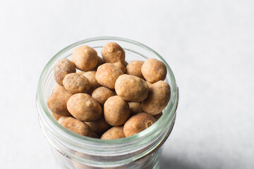 Fried coated peanuts in a glass jar, cracker peanuts on a marble countertop, nigerian peanut snack in a small glass jar