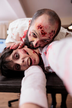 Actors with scary realistic makeup in office horror movie set acting as zombies, consuming flesh. Man covered in scars playing cannibalistic undead monster biting victim, playing in thriller film, POV