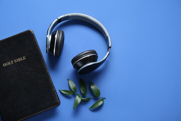 Holy Bible with branch of eucalyptus and earphones on blue background