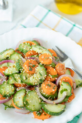 Carrot cucumber red onion salad with sesame seeds and olive oil in plate on white kitchen table. Close-up. Selective focus. Eating healthy homemade raw summer food.