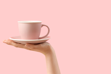 Female hand holding cup and saucer on pink background