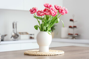 Vase with tulips on table in light kitchen