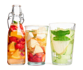 Glasses and bottle of infused water with different sliced fruits on white background