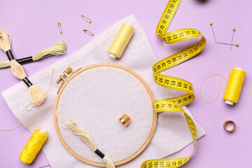 Embroidery hoop with canvas, mouline threads and measuring tape on lilac background