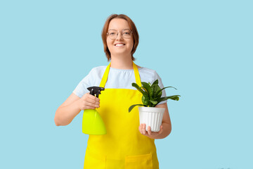 Smiling young woman with houseplant and spray bottle on blue background