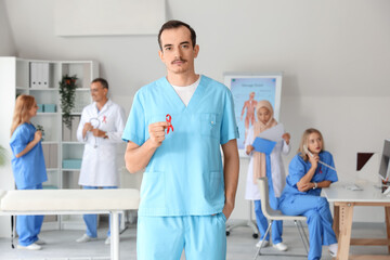 Obraz premium Young male doctor with red ribbon in clinic. World AIDS Day concept