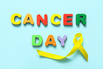 Yellow ribbon and color letters with text CANCER DAY on blue background, closeup. Sarcoma concept.