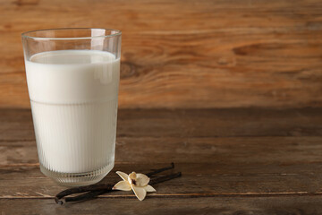 Glass of fresh vanilla milk with sticks and flower on wooden background