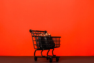 A black shopping cart filled with dark shopping paper bags against a bright red background, black...