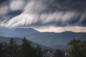 Dramatic view of a hurricane approaching mountainous terrain, with dark, swirling clouds and intense winds.