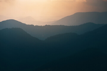 The silhouette of a mountain ridge emerges from the morning fog, with a sunrise pastel sky and the first light of dawn illuminating the landscape