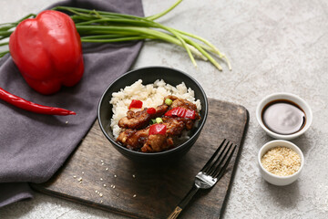 Tasty sweet and sour chicken with rice in bowl, vegetables and fork on grey grunge background, closeup