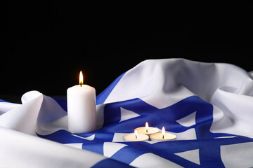 Burning candles and large flag of Israel on dark background. Holocaust Remembrance Day