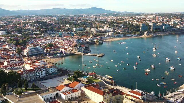 Aerial drone panning over crowded cityscape and Cascais marina in Portugal. From above view of residential area on coast of harbor during sunny day. 