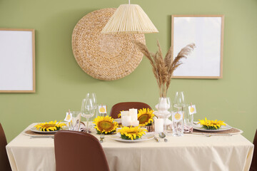 Beautiful table setting with sunflowers in plates near green wall in room