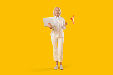 Mature woman with laptop and flag of Spain learning language online on yellow background