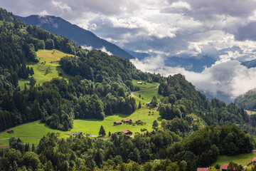 Uma bela vista de algumas casas na encosta de uma montanha com muitas árvores e um céu cheio de...