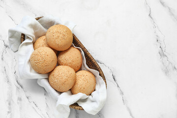 Wicker bowl of fresh buns with sesame seeds on white background