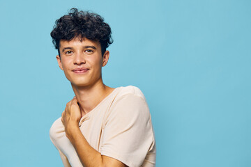 Young man smiling against a light blue background, wearing a casual beige shirt The photo captures...