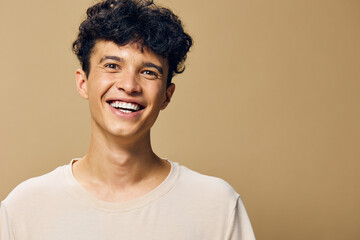 Smiling young man with curly hair in a light beige shirt on a soft brown background, conveying joy and positivity, perfect for lifestyle and happiness concepts