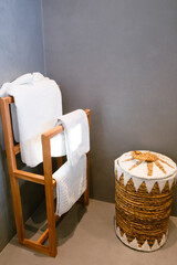 wooden hanger with white towels and straw basket in minimal bathroom interior