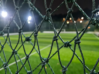 Blurred soccer field or pitch with artificial grass behind the mesh in the sports complex arena in the night.