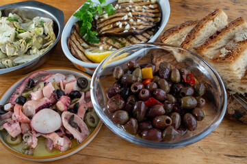 Pickled olives, grilled eggplant, octopus seafood salad, artichokes, vegetables on wooden table, variety of tasty Italian starters, antipasti, tapas