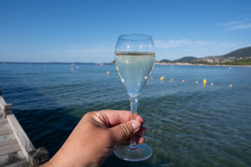 Summer time in Provence, hand with glass of cold champagne cremant sparkling wine on famous Pampelonne sandy beach near Saint-Tropez in sunny day, Var department, France, beach club party